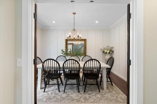 Inviting formal dining room featuring beautiful board-and-batten millwork, hardwood floors, and elegant double doors—an ideal setting for entertaining and special gatherings.