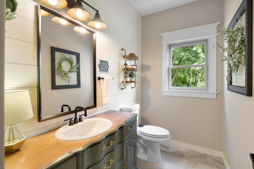 Stylish main-level half bath featuring shiplap accents, custom vanity, statement lighting, and charming designer details.