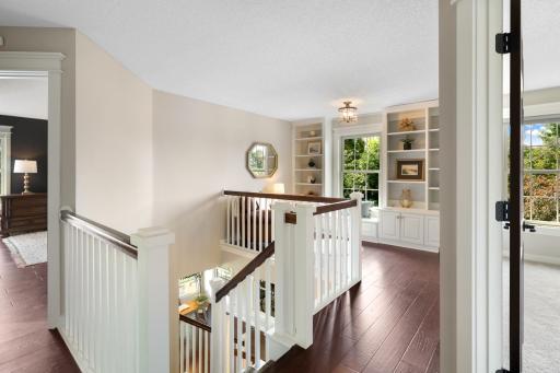 Open upper-level landing featuring rich hardwood floors, custom built-ins, and a bright reading nook/loft overlooking the impressive two-story foyer.