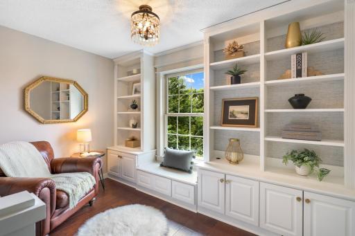 Charming upper-level reading nook featuring custom built-ins, window-seat storage, rich hardwood floors, and peaceful views of the surrounding greenery.