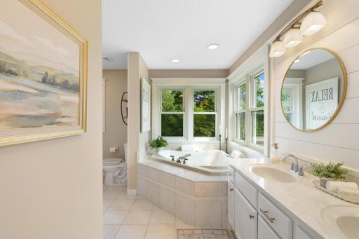 Private primary bath featuring dual vanities, a relaxing soaking tub, abundant natural light, and peaceful views of the surrounding acreage.