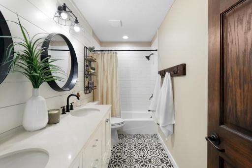 Updated upper-level full bath featuring dual sinks, shiplap accent wall, stylish fixtures, and eye-catching patterned tile flooring.
