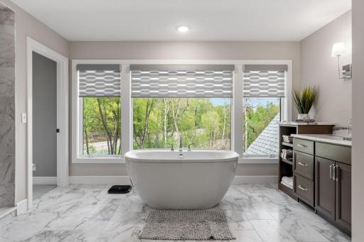 Luxurious Primary Suite w/ auto blinds, spa-like Bath w/ heated floors, freestanding tub, dual vanities & oversized WIC w/ organizational system + pass-through access to Laundry