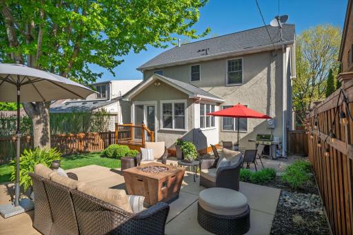 The backyard patio is an outdoor living room. Lush landscaping, a fire pit, generous seating, and a sunroom backdrop create the perfect setting for summer evenings in Highland Park.