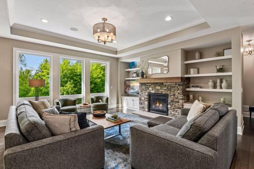 The inviting Great Room features a box vault ceiling with enameled crown molding and floor-to-ceiling windows that look out to the wooded backyard.