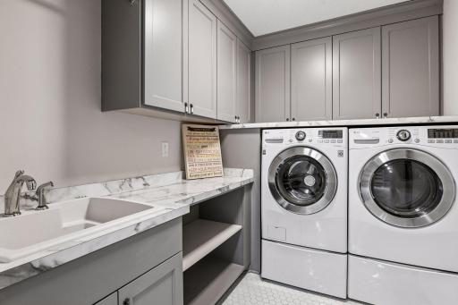 Upper-level tiled laundry room with sink, storage, shelves and upper laundry for convenience.