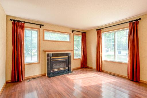 Bright and inviting living room featuring abundant natural light, warm flooring, and a cozy gas fireplace as the focal point.