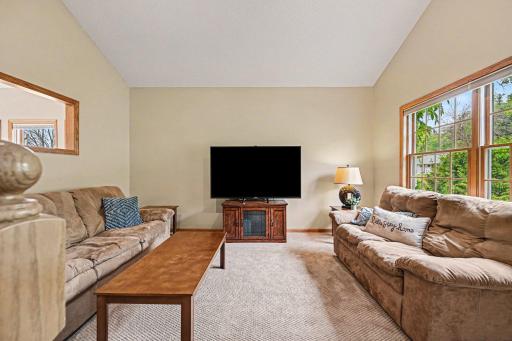 Filled with natural light from large front windows and a wall opening to the sunroom, this formal living room impresses with its dramatic vaulted ceiling, elegant recessed lighting, and bright, airy atmosphere.