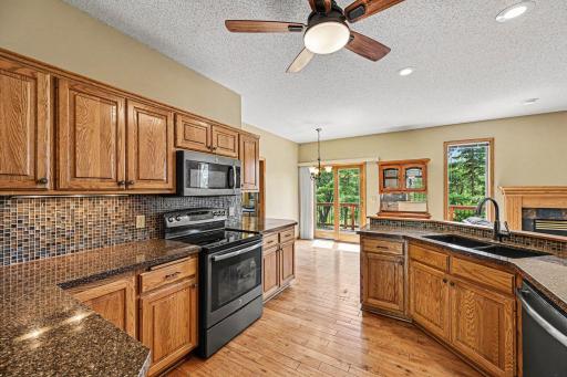 Viewed from the dining room, this kitchen shines with hardwood floors, abundant oak cabinets, and granite countertops with a glass tile backsplash. Features include ample counter space, canned lighting, and a ceiling fan.