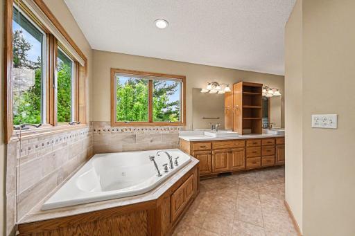 Relax the day away in your own jetted soaking tub! This view highlights the tub with its beautiful ceramic tile surround, the bright corner windows, and the extra-large vanity packed with tons of storage.