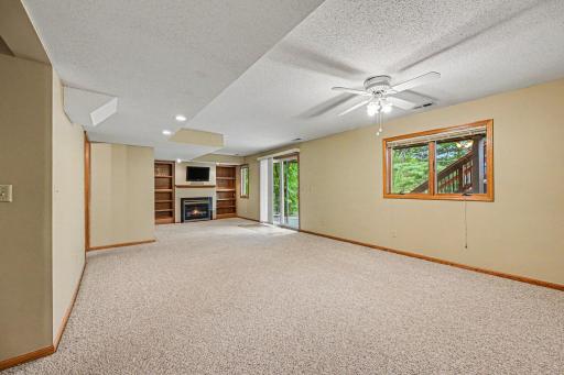 The finished lower-level walkout leads straight to a private backyard patio and firepit! This cozy rec room features custom built-in bookcases, a warm gas fireplace, modern canned lighting, and a cooling ceiling fan.