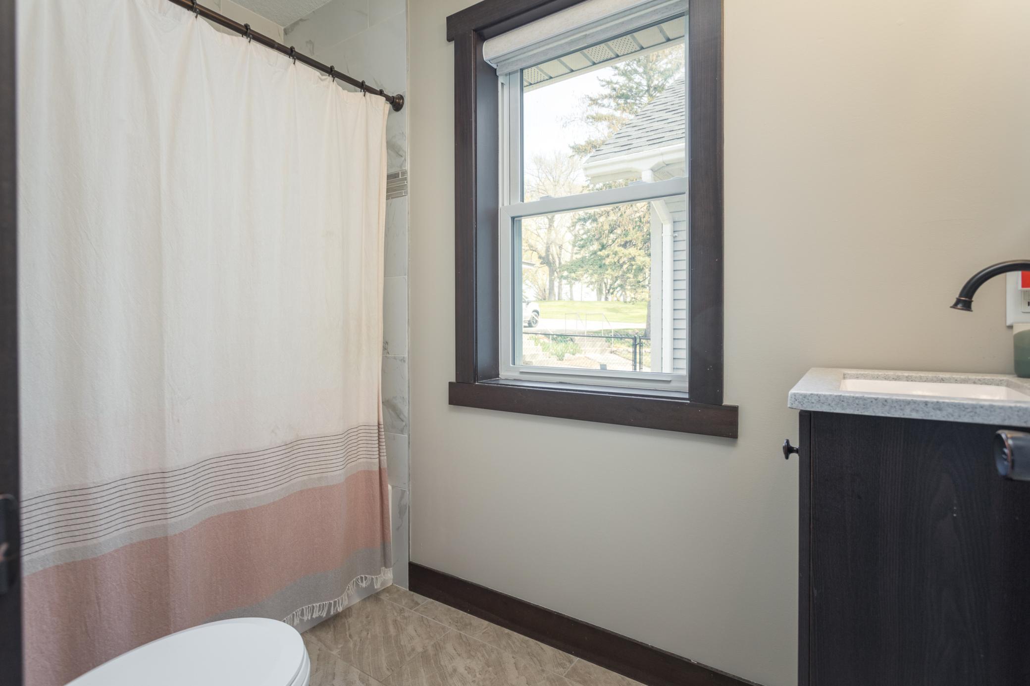 Charming bathroom with a bath-shower combo, marble-inspired shower backsplash, and a window that fills the space with natural light