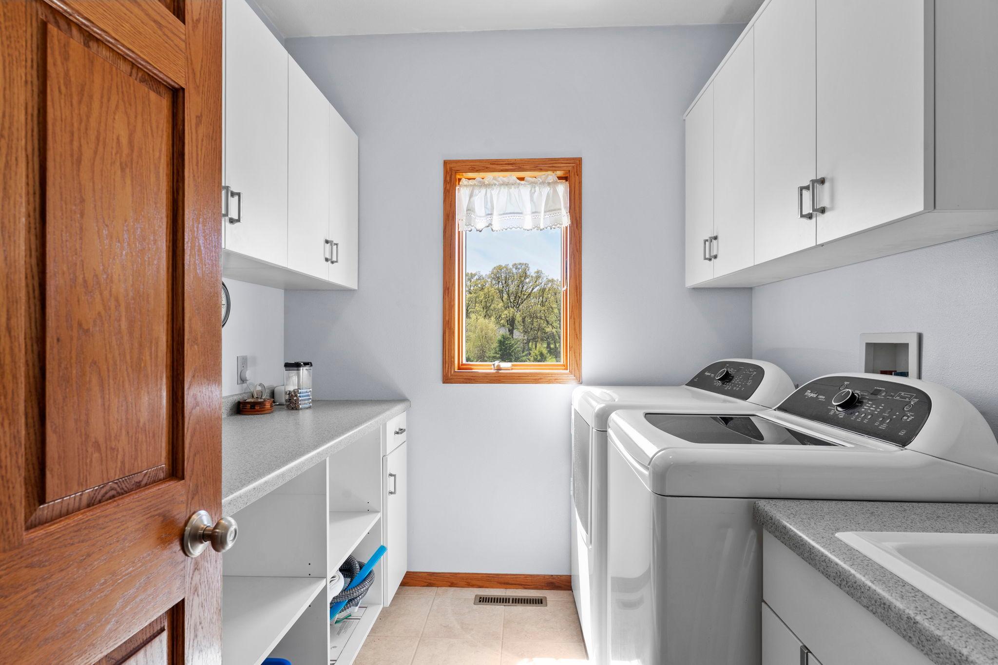 The finished laundry room features thoughtfully designed storage with cabinetry, cubbies, a utility sink, and hanging racks.