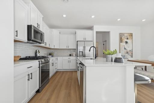 Photo is of the actual model. This spacious kitchen includes a large center island, quartz countertops, recessed lighting, LVP wood floors, stainless appliances and more.