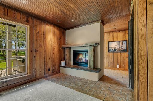 Impressive lower-level layout featuring a two-sided fireplace with a custom driftwood mantle, tile accent flooring, and rustic wood walls