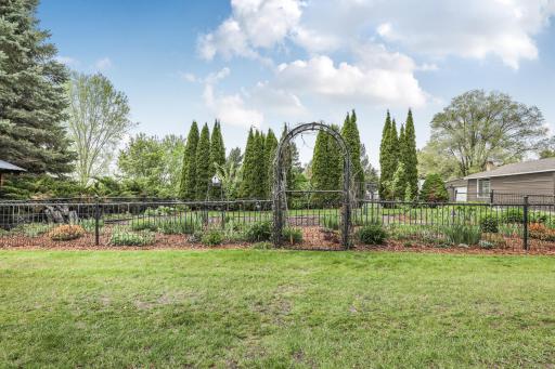 A charming iron arbor serves as the entryway to a beautifully manicured, fenced-in perennial flower garden.