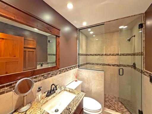 Beautifully finished lower-level bathroom with tile work, granite countertops, and plenty of storage.