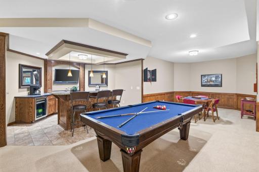 Warmth surrounds this lower level, with wood wainscoating on the walls , built-in cabinetry in bar area with refrigerator and detail surround around the TV