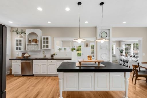 The kitchen features abundant white cabinetry, generous counter space, a spacious center island for additional prep space and stylish pendant lighting, stainless steel appliances, a cooktop with exhaust hood, and a convenient walk-in pantry closet.