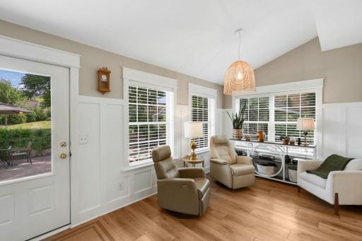 Adjacent to the dining room is a charming sitting area filled with natural light and accented by a stylish hanging light fixture, wainscoting, trim, and built-in shelving, with direct access to the spacious backyard patio.