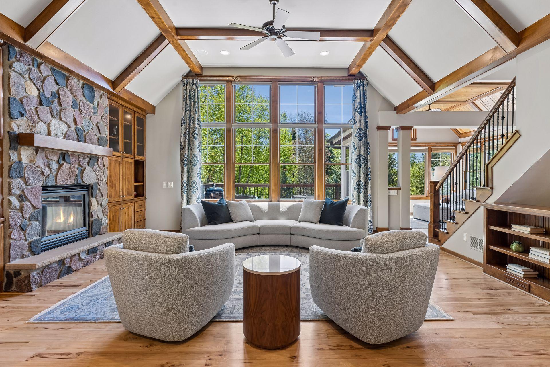 Gorgeous grand formal living room with a vaulted coffered ceiling and alder wood beams, hickory floors, a wall of windows overlooking the stunning backyard, built-in cabinets & shelves, a ceiling fan & a stone gas fireplace complete the room.