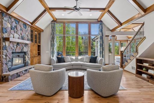 Gorgeous grand formal living room with a vaulted coffered ceiling and alder wood beams, hickory floors, a wall of windows overlooking the stunning backyard, built-in cabinets & shelves, a ceiling fan & a stone gas fireplace complete the room.