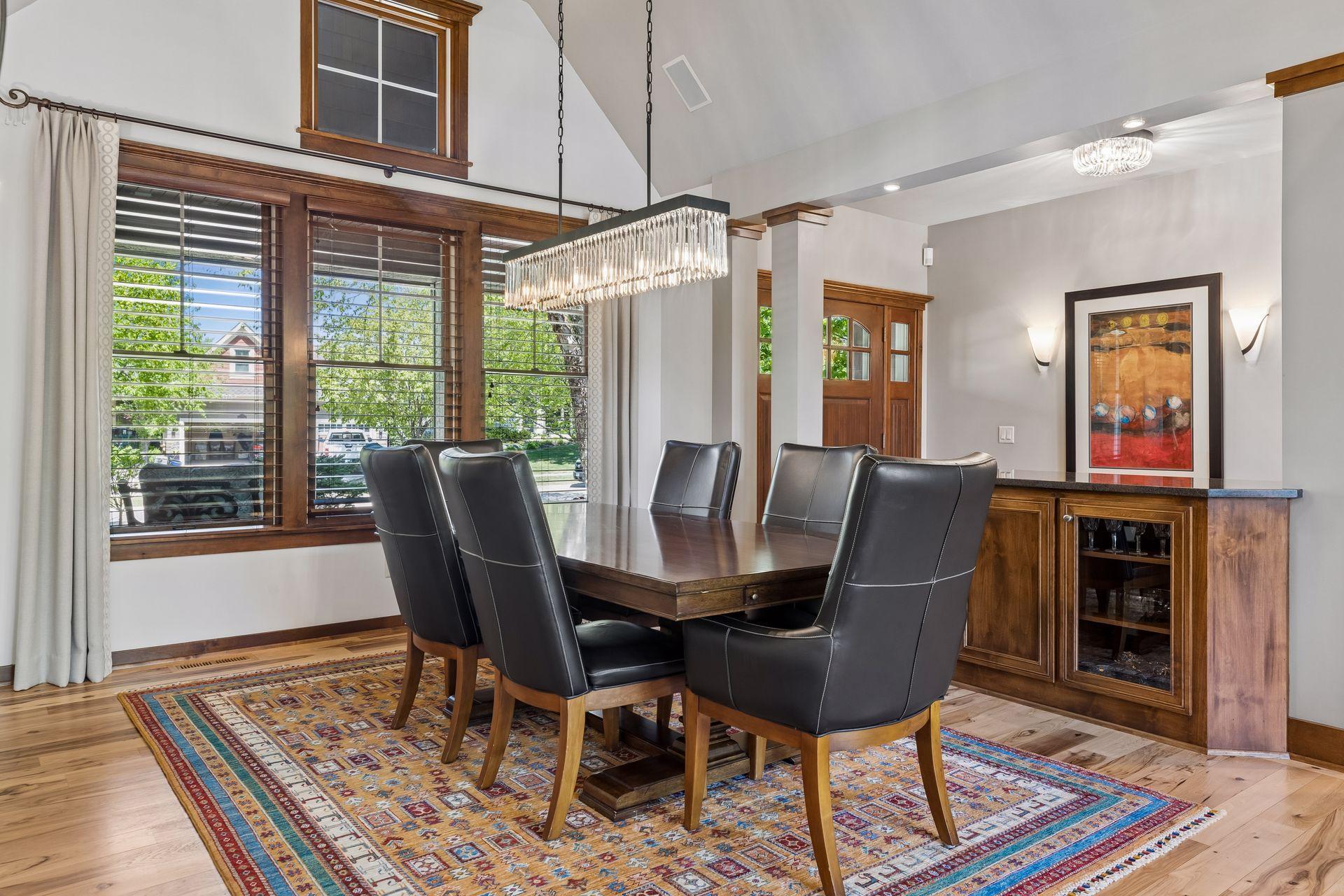 The formal dining room features a vaulted ceiling with a large window and a shadowbox window, a built-in buffet with a granite countertop, a storage cabinet with glass doors, wood blinds, and a new light fixture - 2025.