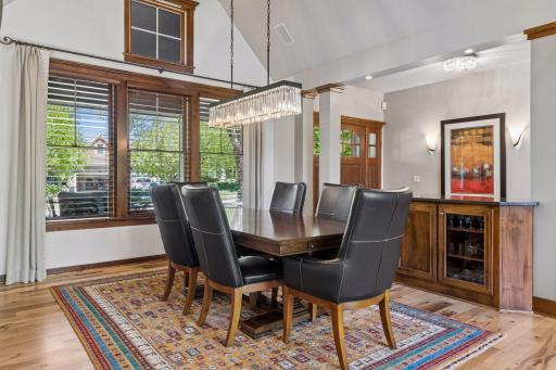 The formal dining room features a vaulted ceiling with a large window and a shadowbox window, a built-in buffet with a granite countertop, a storage cabinet with glass doors, wood blinds, and a new light fixture - 2025.