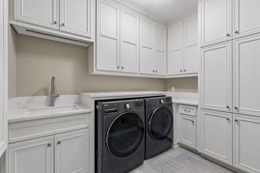 Laundry day won't be a chore in this laundry room. It features abundant storage cabinets, ceramic tile floors, front-load LG ThinQ washer & gas dryer w/folding counter, an extra-deep utility sink, built-in iron board & genius pull-out drying racks.