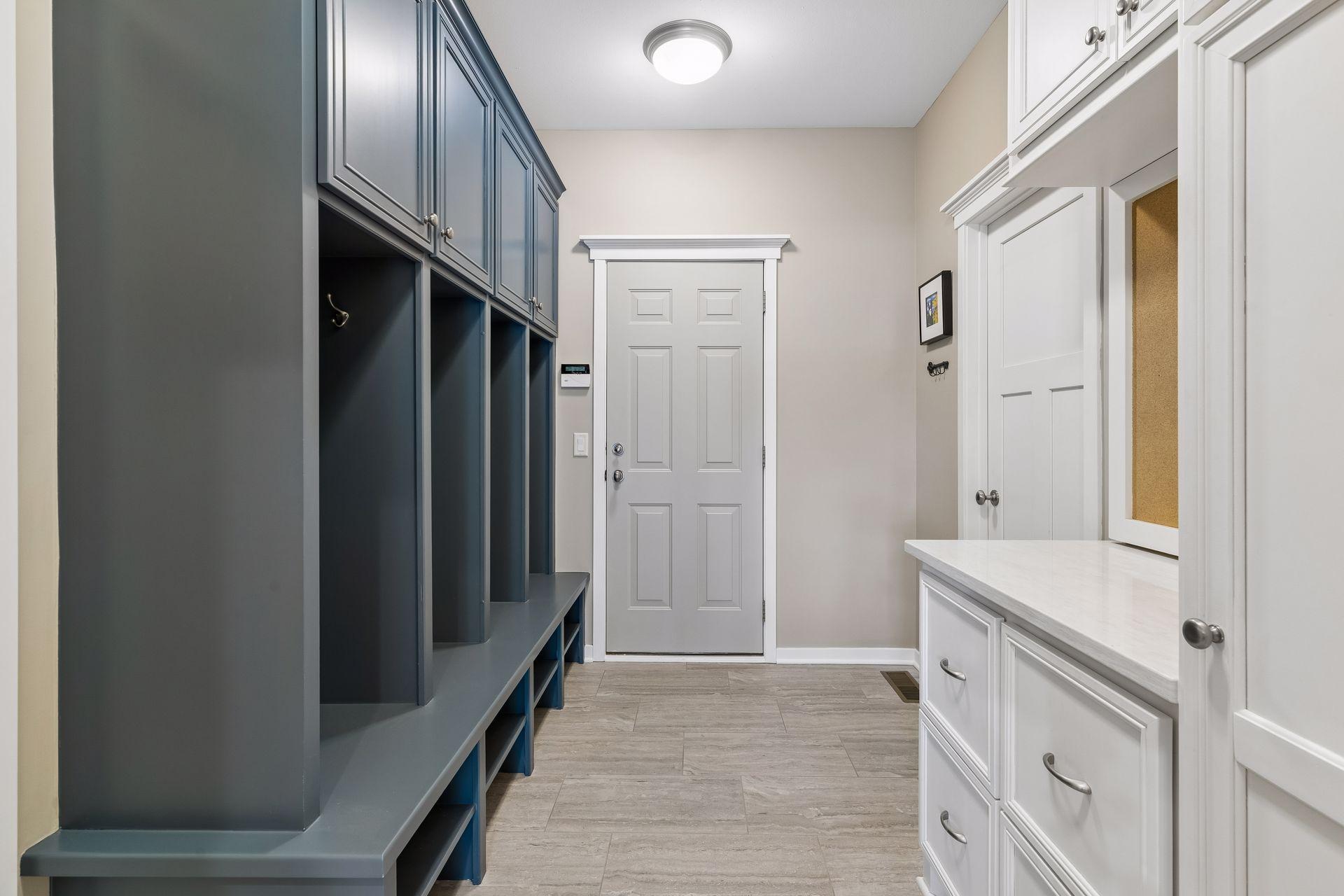 The mudroom is conveniently located between the garage & kitchen. It features built-in lockers w/storage, a large coat closet, ceramic tile floors, quartz countertop, built-in cabinets w/storage & a corkboard central command communiation center.