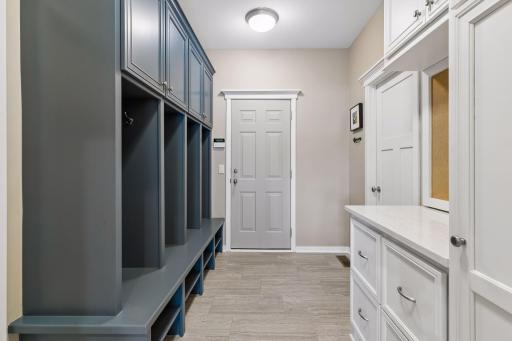The mudroom is conveniently located between the garage & kitchen. It features built-in lockers w/storage, a large coat closet, ceramic tile floors, quartz countertop, built-in cabinets w/storage & a corkboard central command communiation center.
