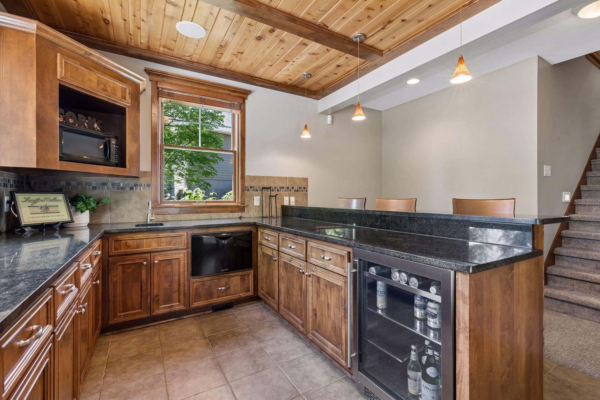 The bar includes loads of cabinets, a dishwasher, a sink, a microwave & a new beverage refrigerator (2025). It's lit w/pendant & recessed lights, is wired for surround sound, ceramic tile backsplash, granite countertops & a door to the paver patio.