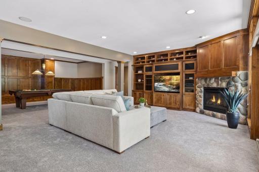 The spacious lower-level family room is designed for relaxation or entertainment. A large patio door surrounded by windows leads out to the backyard & the room includes built-in shelves & storage, & a stone gas fireplace. F