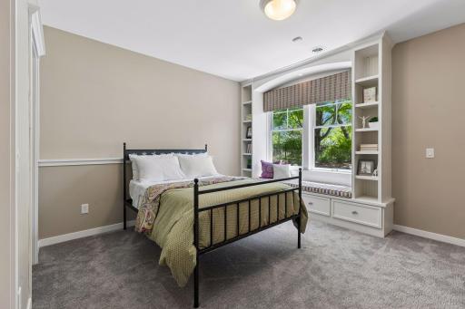 Bedroom 3 in the lower-level includes a custom-built-in window seat with bookshelves and storage. It overlooks the gorgeous backyard oasis.