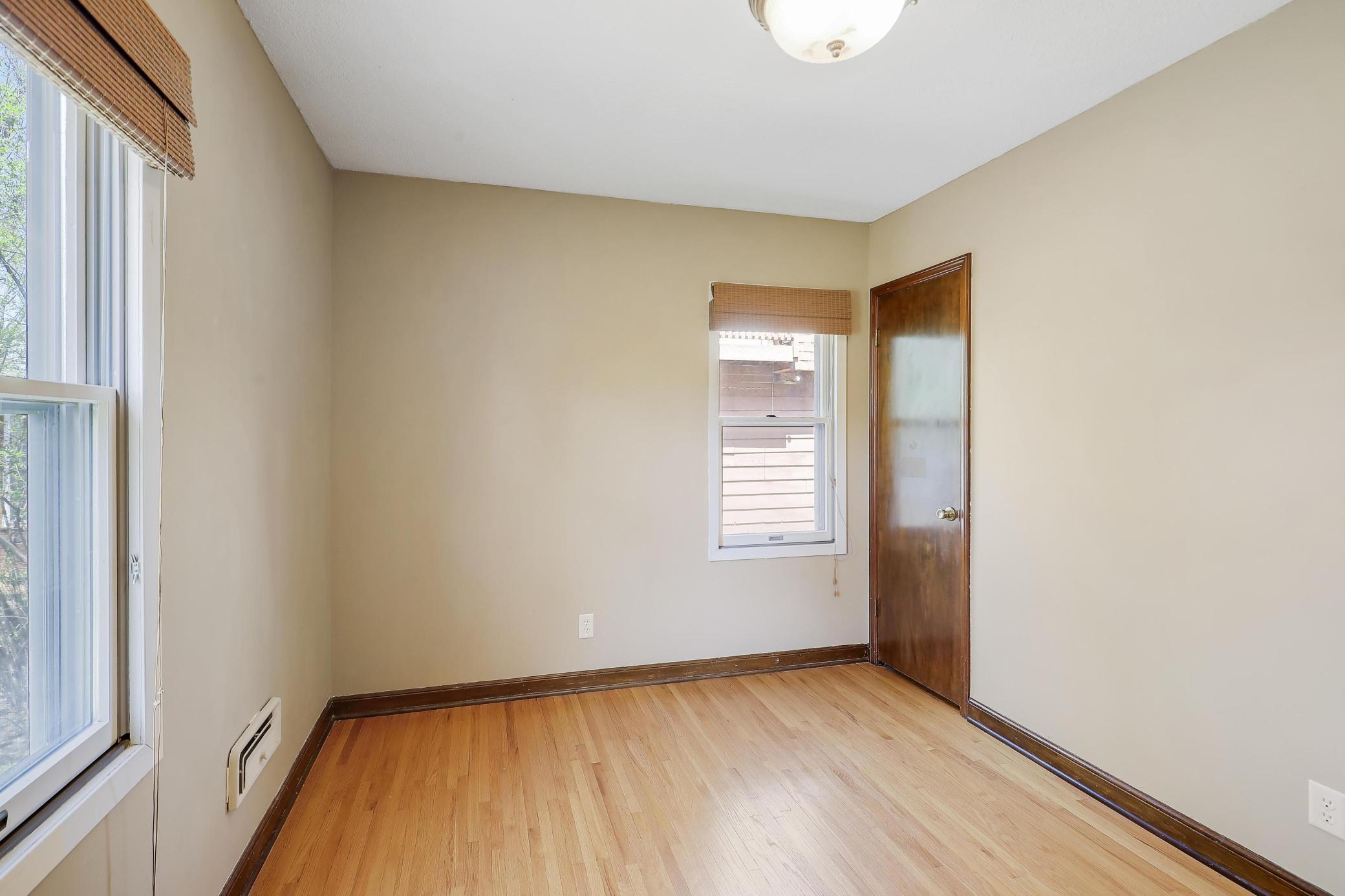 Another look at the secondary bedroom in the main level. Showcase hardwood floors, wood millwork and privacy blinds.