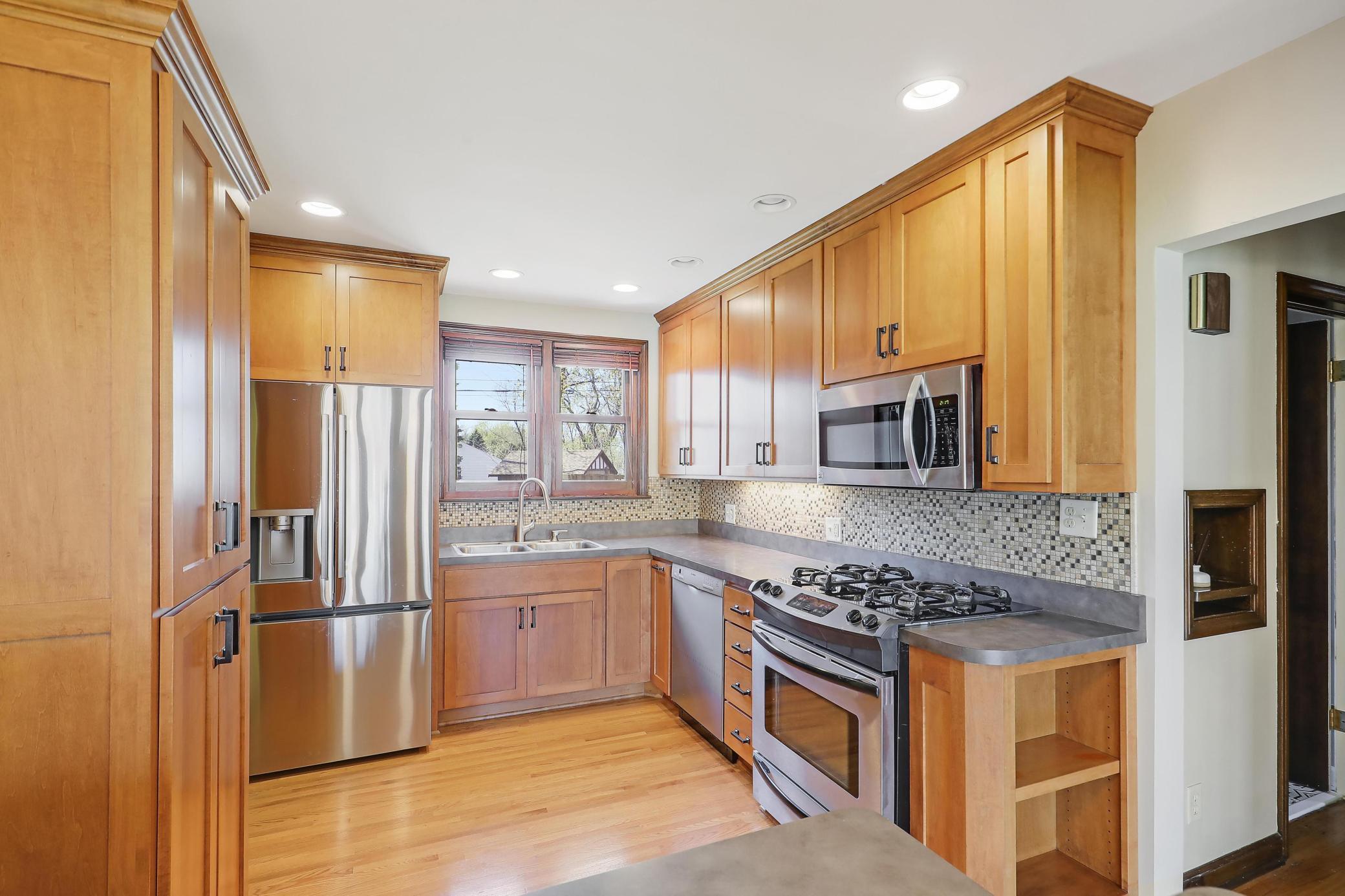 New French armoire-style refrigerator, wood cabinetry with black metal hardware and glass tile backsplash add finesse to this kitchen.