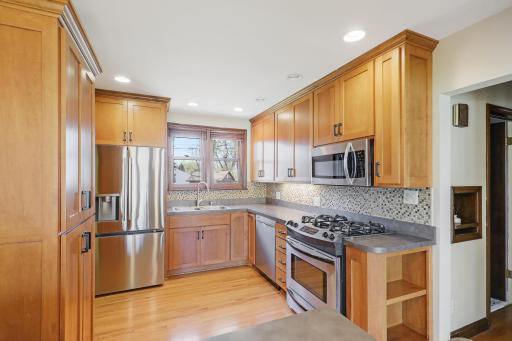 New French armoire-style refrigerator, wood cabinetry with black metal hardware and glass tile backsplash add finesse to this kitchen.
