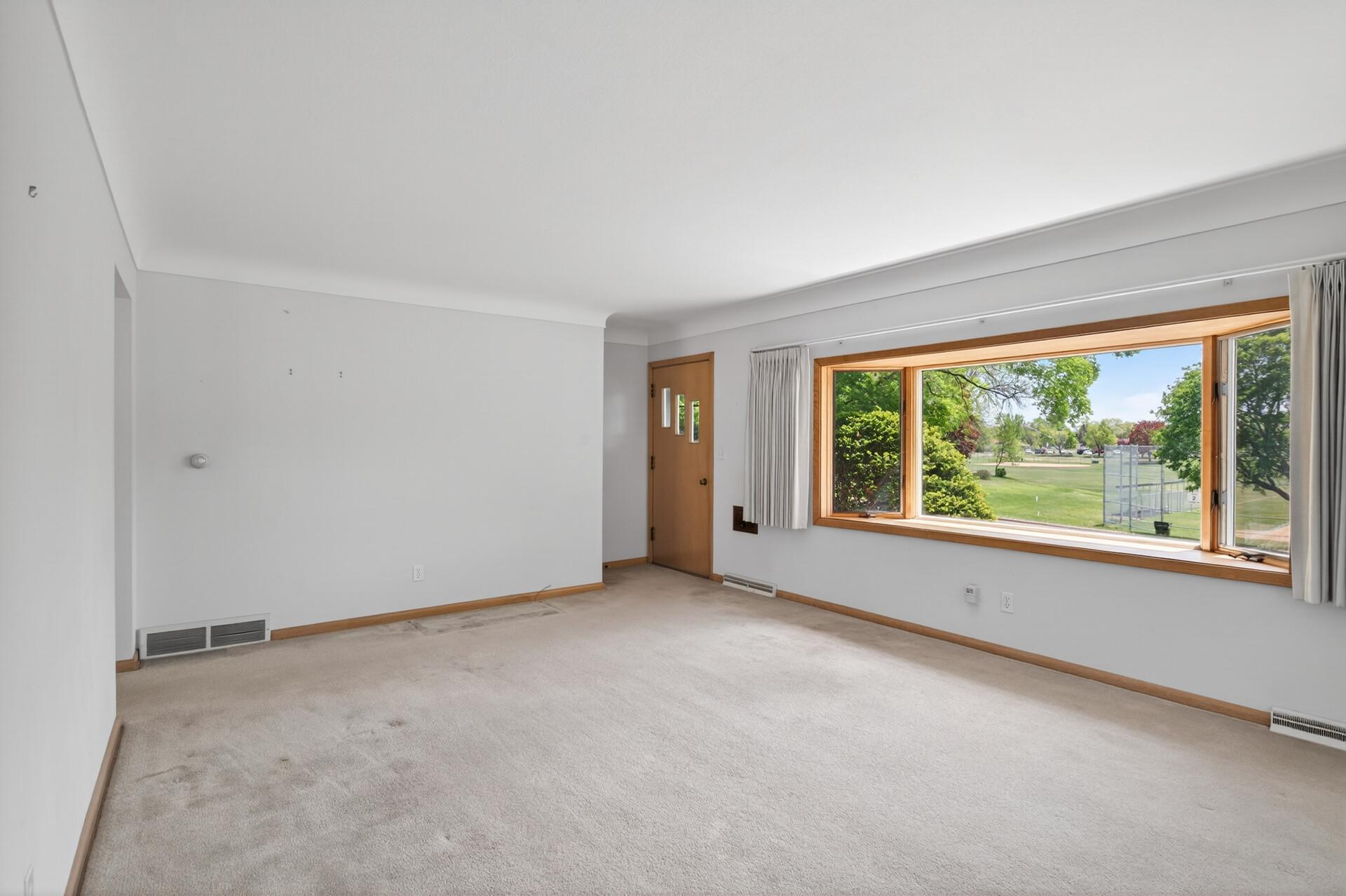 Large front facing living room with coved ceiling, big bowed window looking out at a city park.