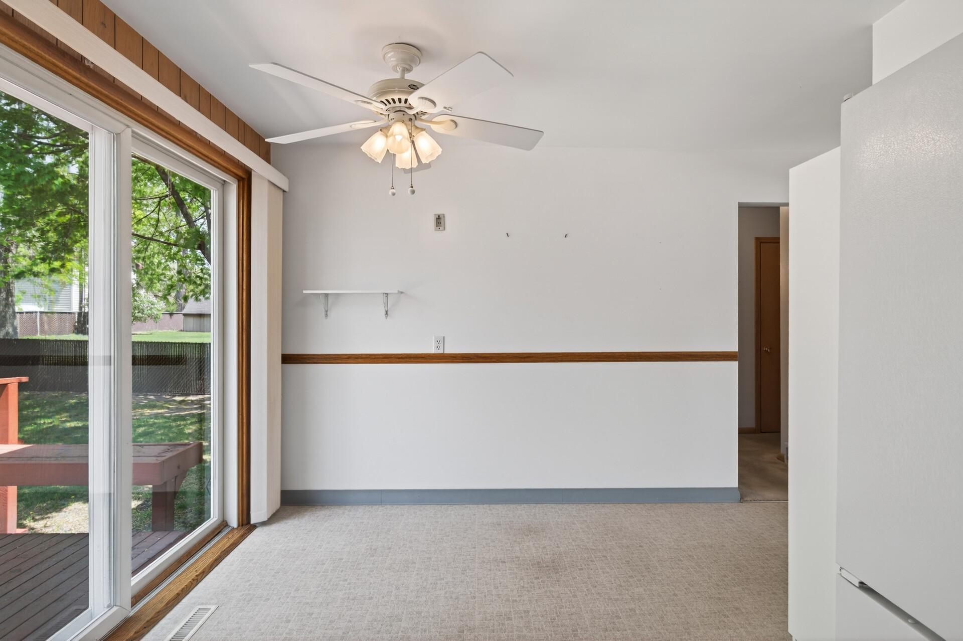 Informal dining area with a ceiling fan off the kitchen with a newer sliding glass door out to a deck.