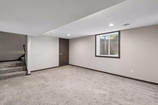 Spacious lower-level family room with fresh finishes and ample space to relax or entertain. The perfect setup for movie nights. The egress windows add natural sunlight to the space. There is extra storage located under the stairs.