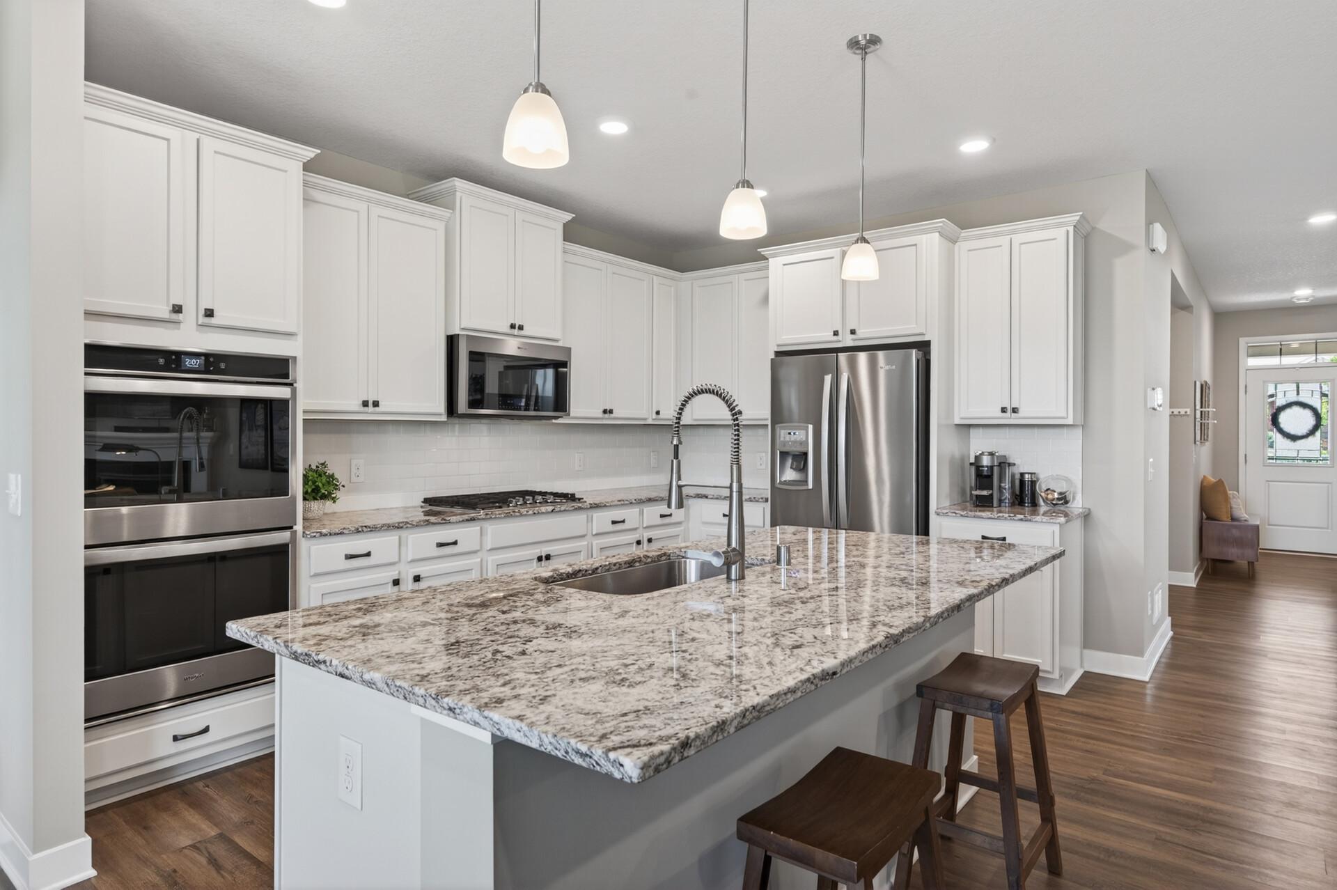 Crisp white cabinetry kitchen with large granite countertops with bar stools, white backsplash and stainless steel refrigerator with filtered water. Don't miss the walk-in pantry in the hallway.