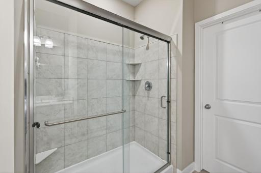 Spa-like shower with pristine tile surround, corner built-in bench and shelving for products.