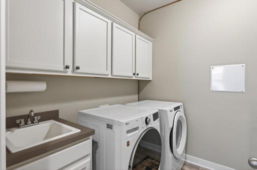 Steps away from the primary suite is this separate laundry room with sink, front load washer, front load dryer, and upper cabinetry. Also, your mechanical room with Air-to-Air exchanger, water softener and humidifier.