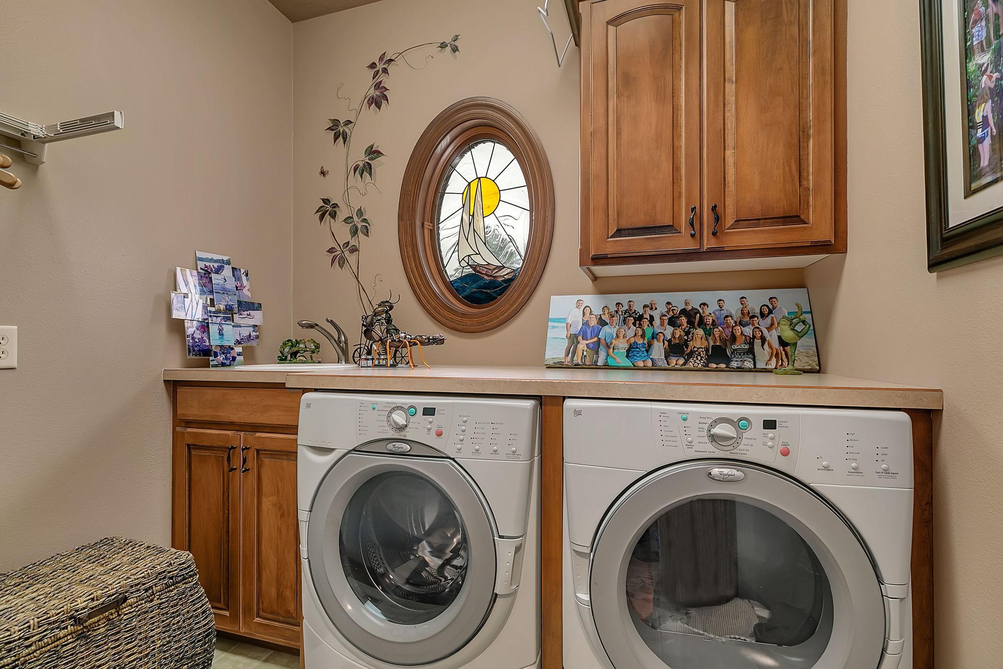 Main Level Laundry with counter space, raised panel cabinetry, utility sink, all made pleasing by a cheerful oval stainglass window.