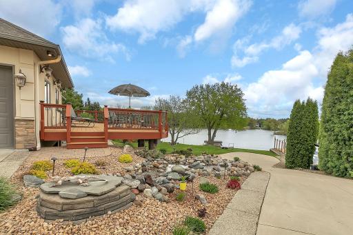 Serene waterfall winds through the landscape, creating a tranquil setting. Deck space wraps from slider at the dining room around the garage. To concrete on the right is the driveway access to the lower tuck under garage.