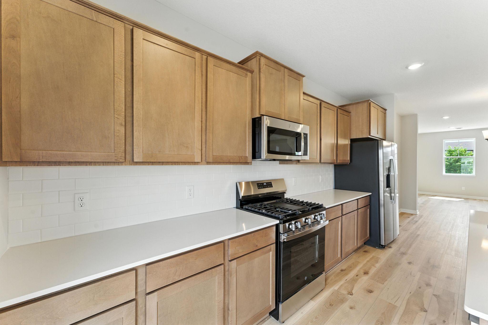 It's all in the details...quartz countertops, tile backsplash & stainless appliances. Notice the amount of surface space & cabinets! The 6' island provides add'l seating for causal dining. Similar home shown, options can vary.