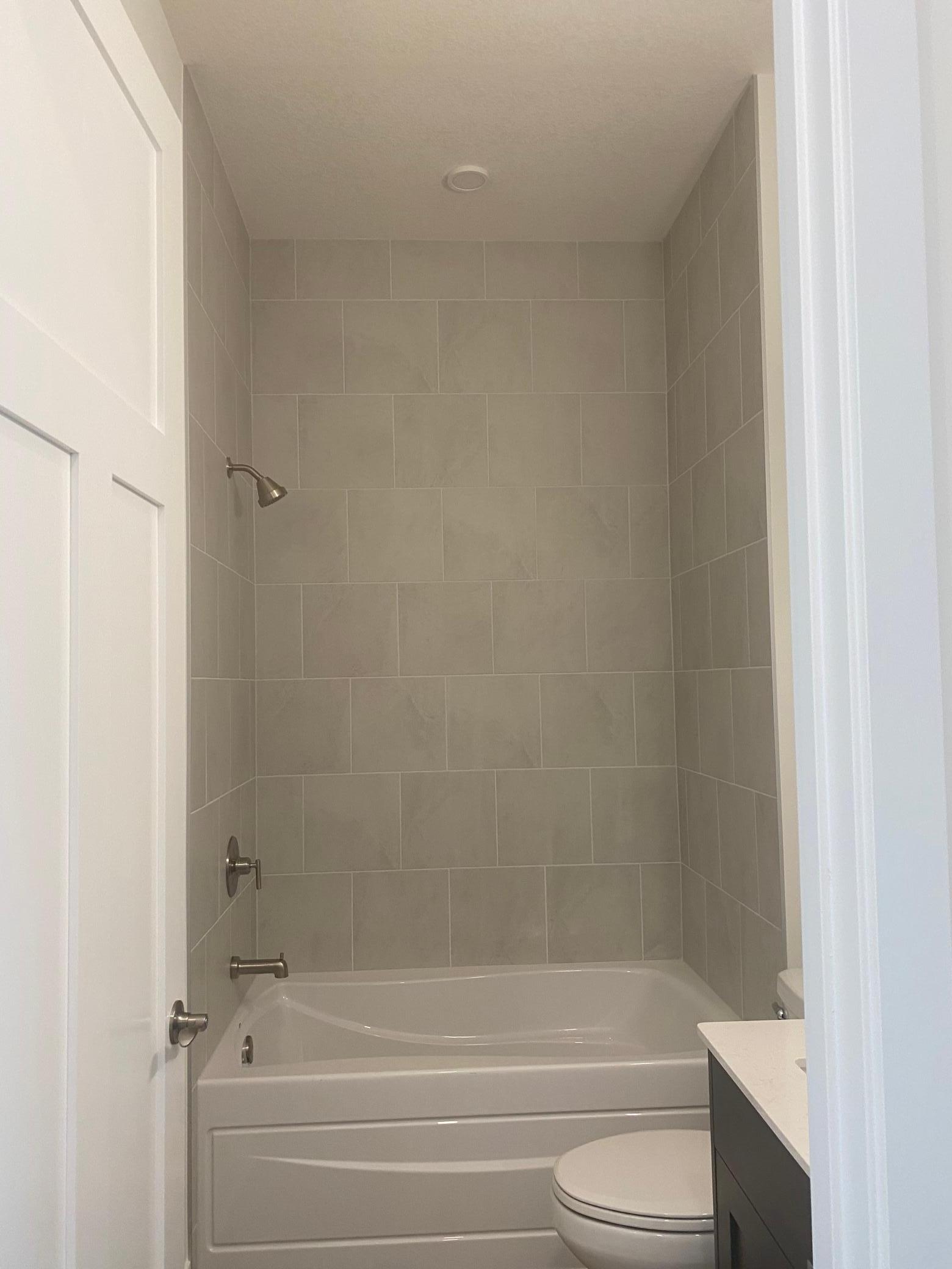 Main bath features a floor-to-ceiling tiled shower paired with a tub/shower combo—style and versatility in one space.