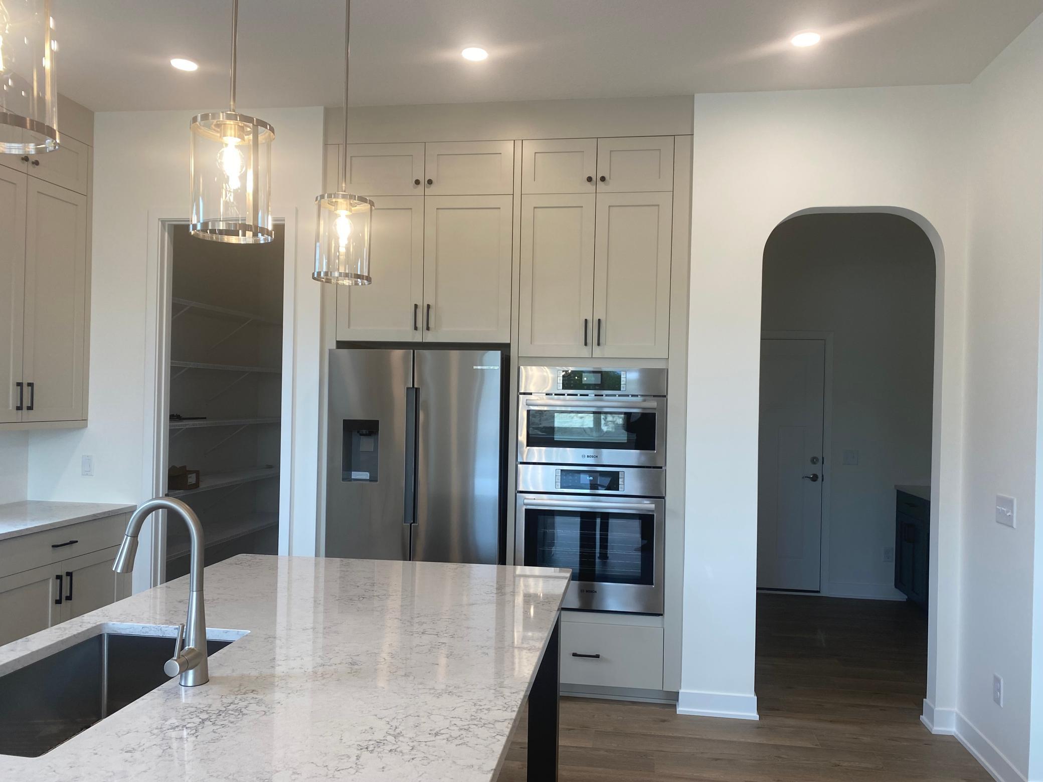 Gourmet kitchen highlights Bosch fridge, built-in microwave and wall oven, plus an elegant arched entry to the mudroom—style and function seamlessly combined.