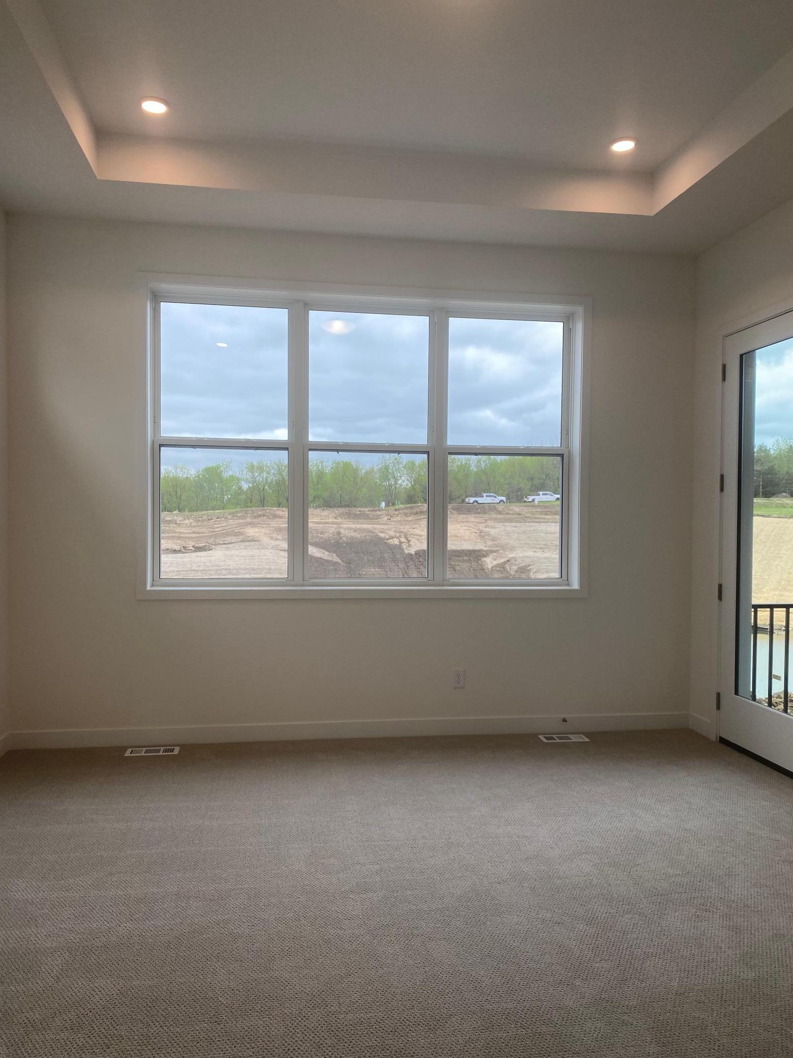 Primary bedroom with oversized windows overlooking the pond and a dramatic box-vaulted ceiling—bright, airy, and serene.