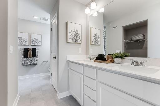Primary bathroom offers a raised vanity with 2 sinks, Quartz counters and linen storage. *Model home, colors and finishes will vary.